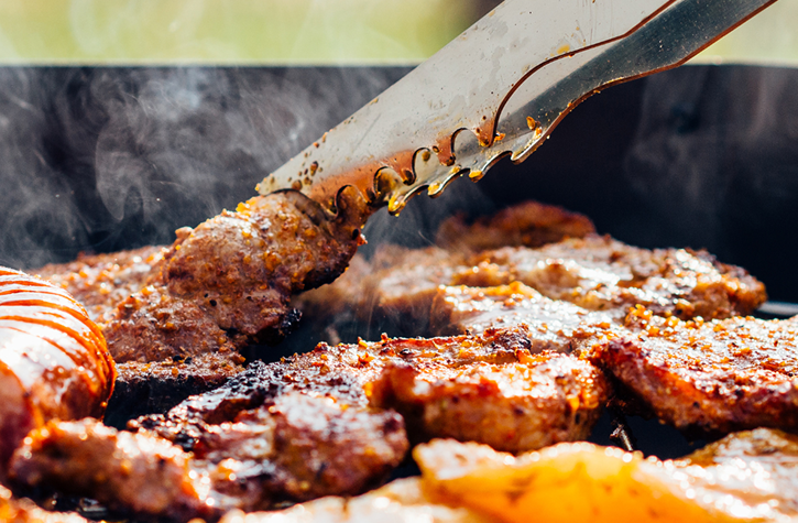Viande en train d'être grillée et retournée sur un brasero de cuisson